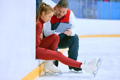 Male coach talking to young female figure skater.