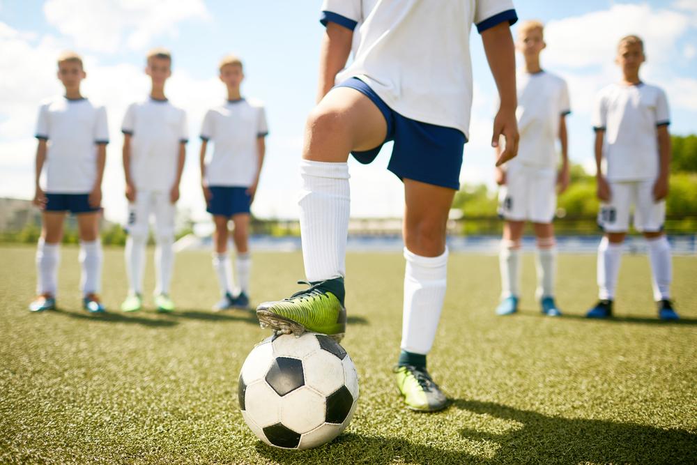 Captain of soccer team viewed from waist down standing in front of other team members.