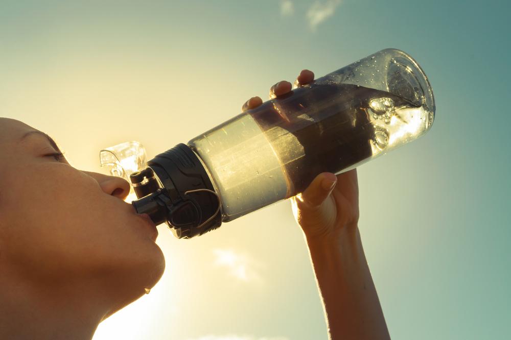 Close up of young woman drinking water out of reusable bottle.