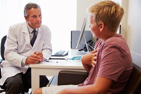 A young teen boy talking to his doctor in an office.