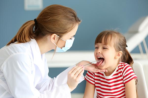 A female doctor putting a tongue depressor in a young patient's mouth.