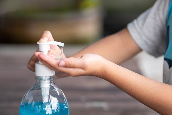 Close-up of a white child pumping hand sanitizer from a large container.