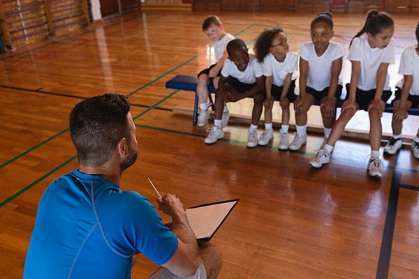 Coach talking to a diverse group of kids in a gym.