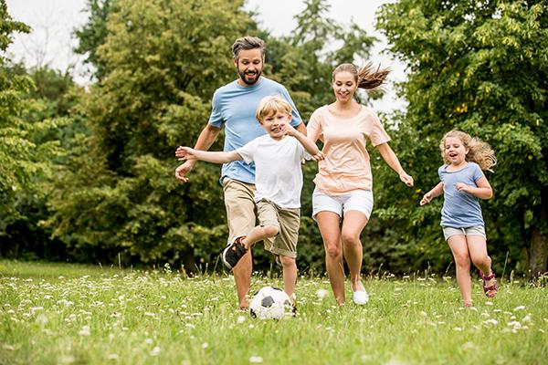 A white couple playing soccer outside with two children.