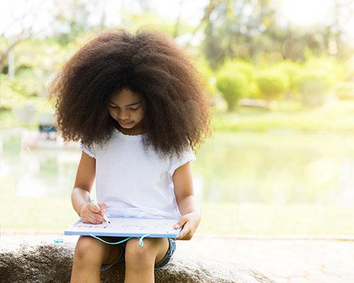 Young black girl writing on a white board outside.