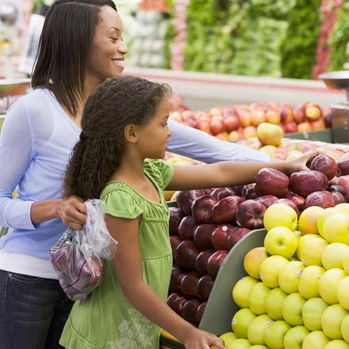 A black other and daughter picking out apples at a grocery store.