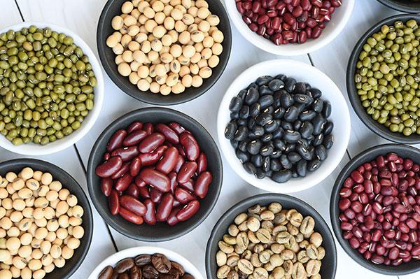 bowls of different types of bean on white wood table