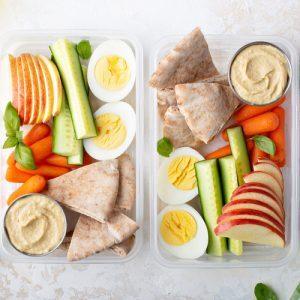 Hummus with veggies and fruit and hard boiled egg in plastic containers.