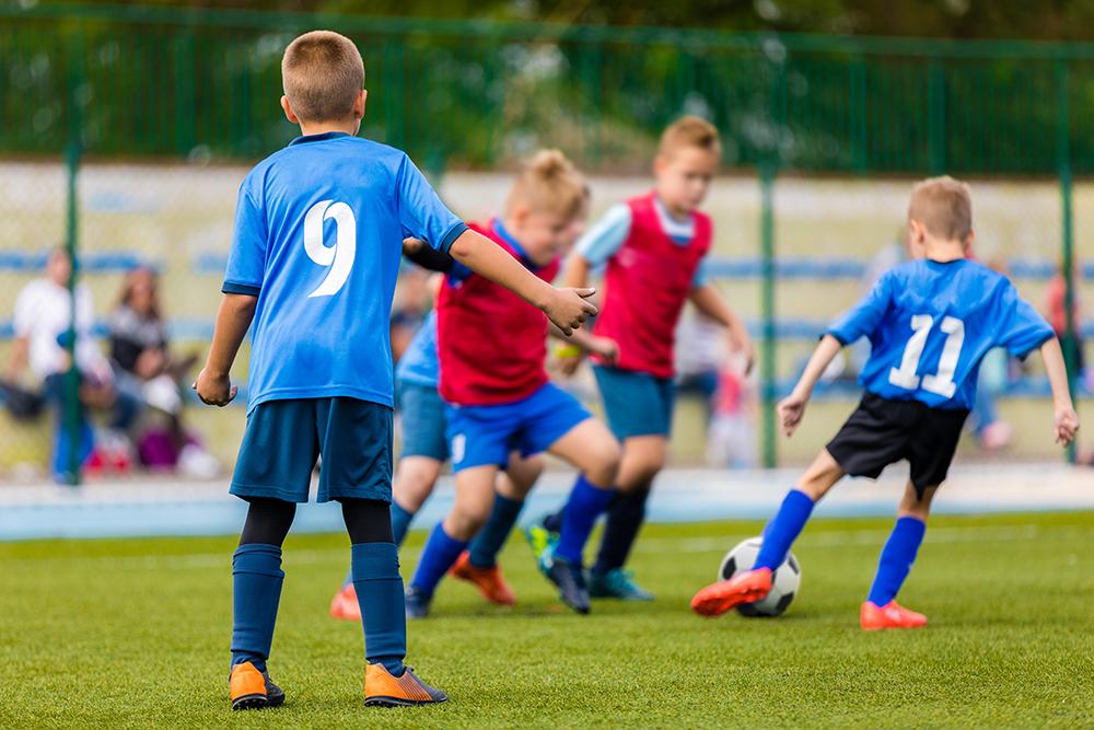 Soccer players on the field, boy player watching as others have ball.