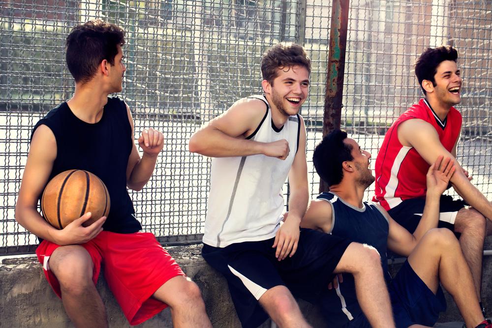 Small group of young men laughing next to basketball court.