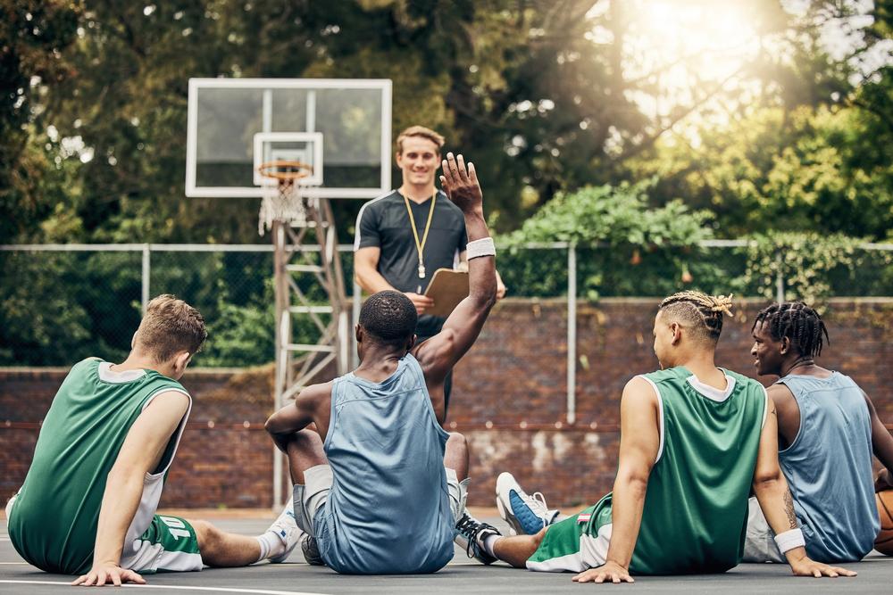 Coach talking to youth men basketball team on outdoor court.