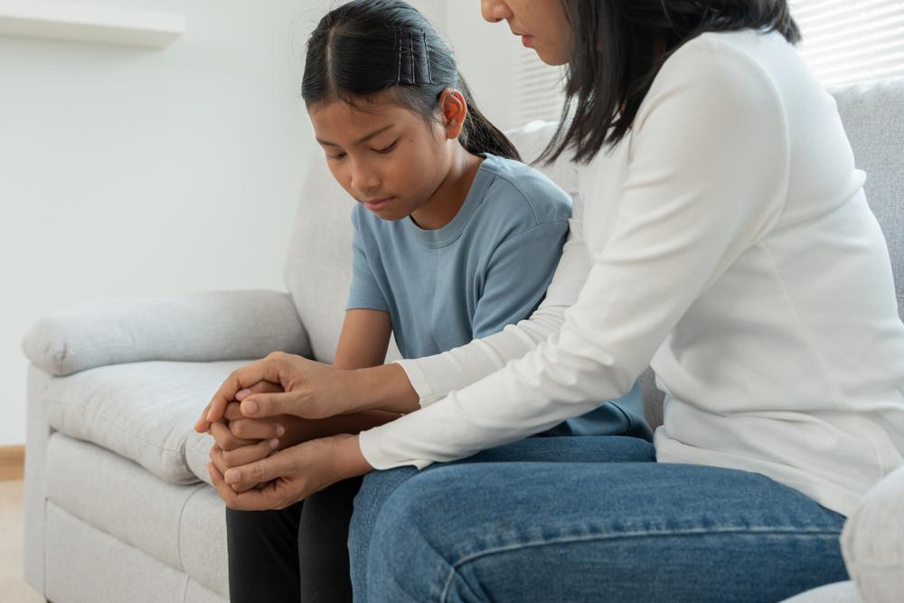 Mom sitting with daughter and holding hands on a couch.