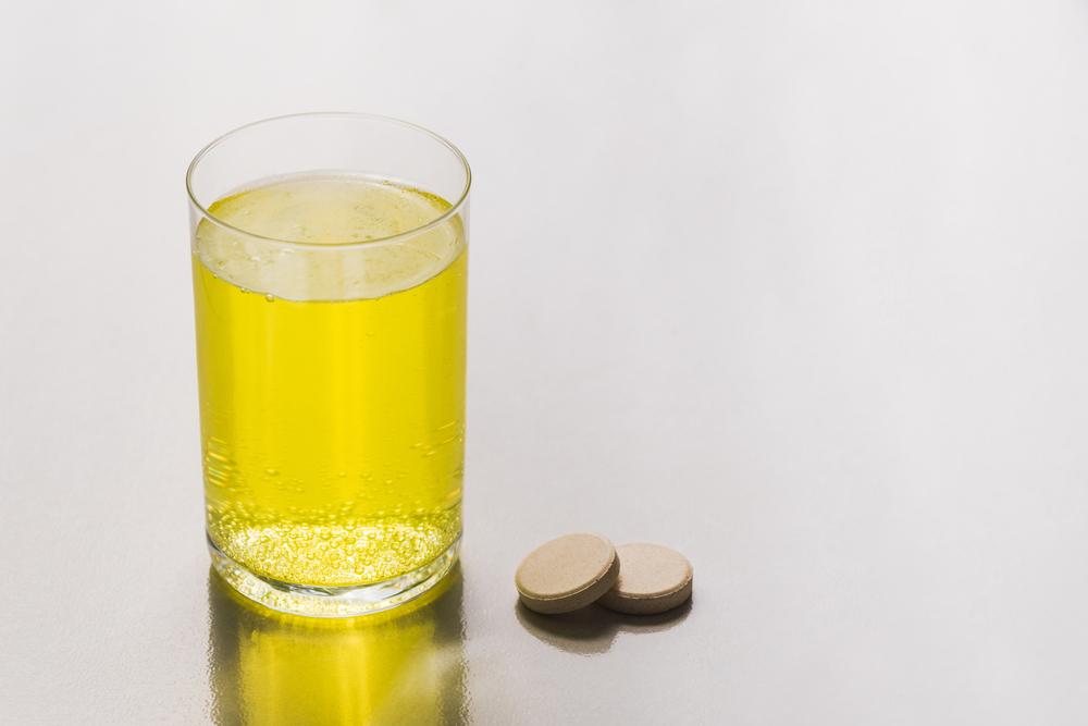 A glass of orange fizzy liquid next to two dissolvable tablets.