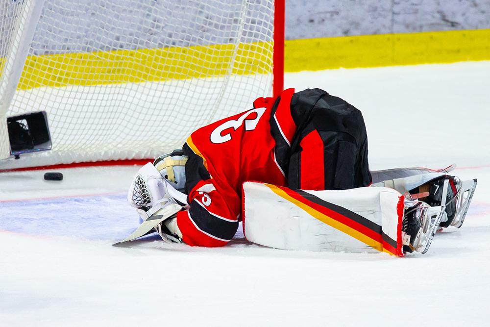 An upset hockey goalie on hands and knees facedown.