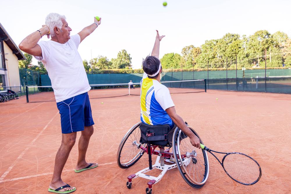 Coach with wheelchair tennis athlete on court.