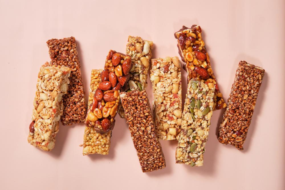 A variety of process granola bars out of their packaging against a pink background.