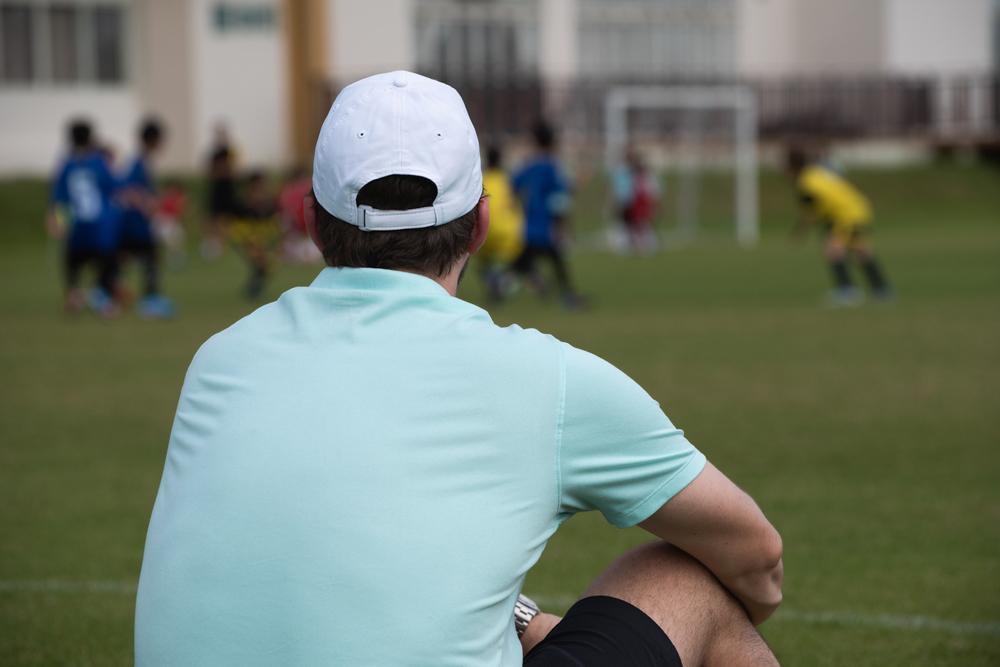 Dad sitting on sidelines of youth soccer game.