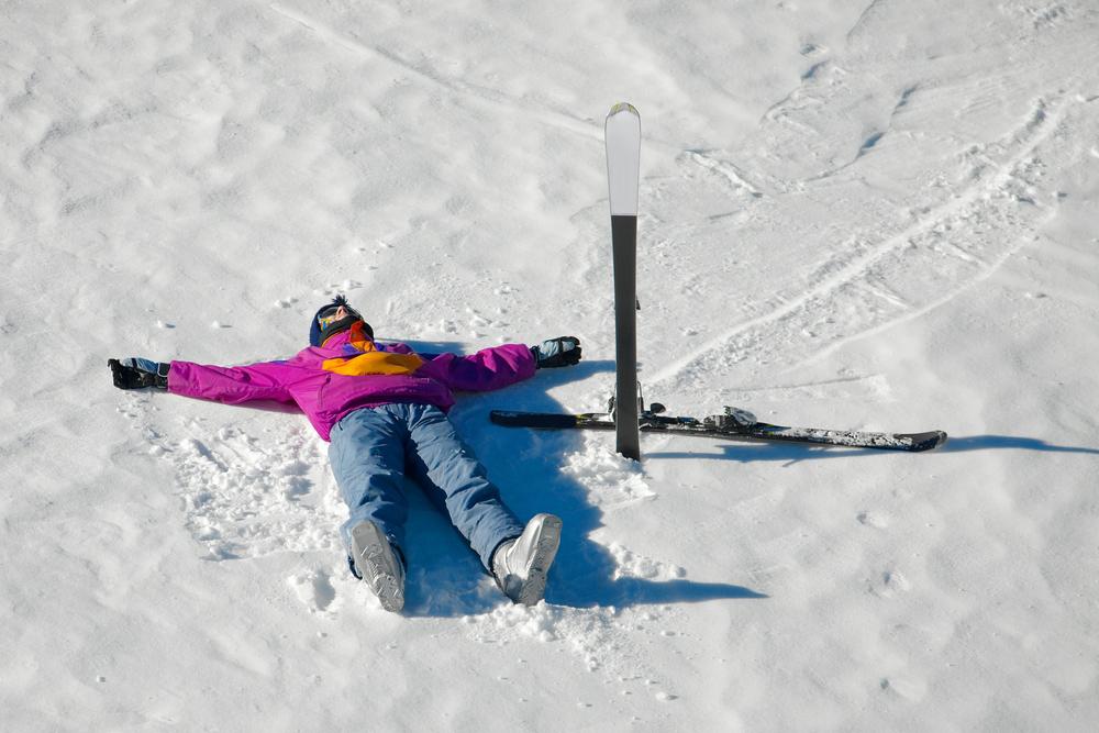 Skiier laying down on snow with skis next to them.