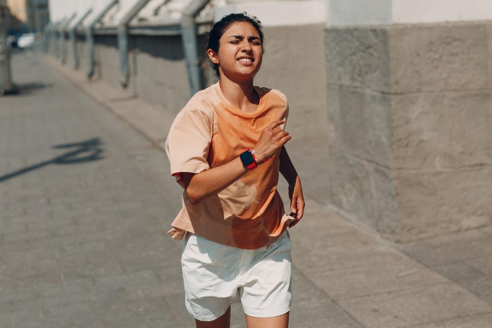 Young woman running outside with a sweat soaked shirt.