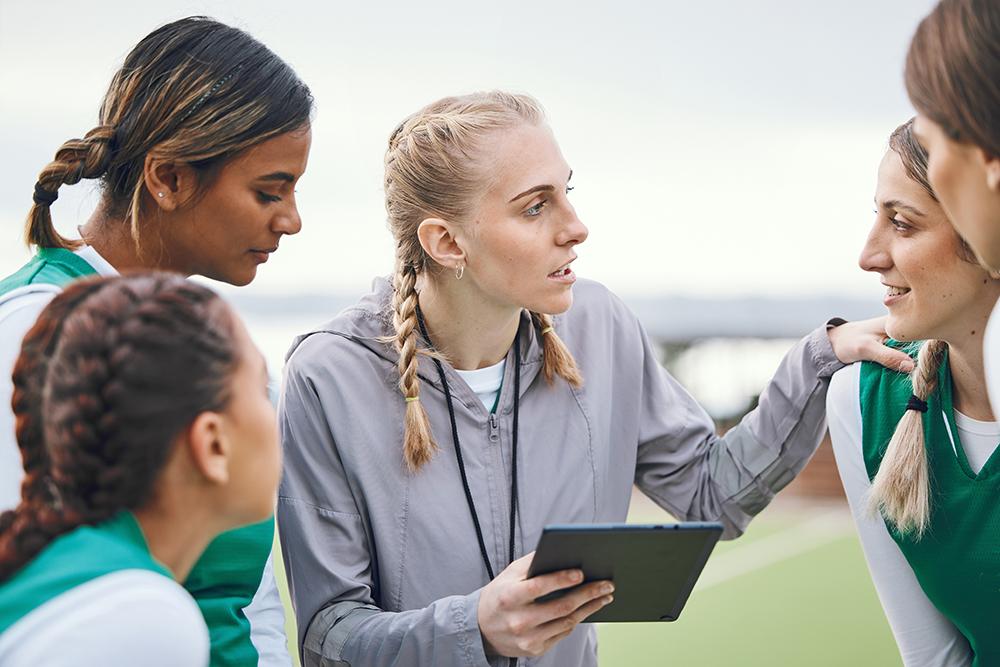 Female coach talking to youth athlete team on field.
