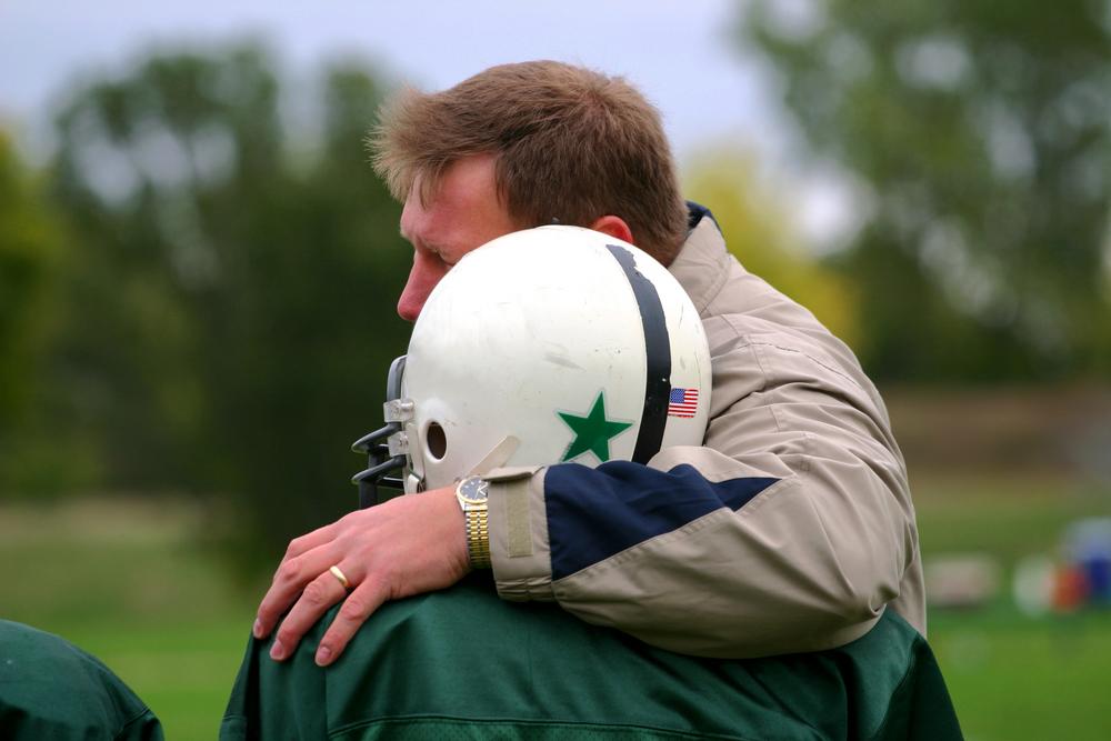 Dad comforting son wearing football helmet.