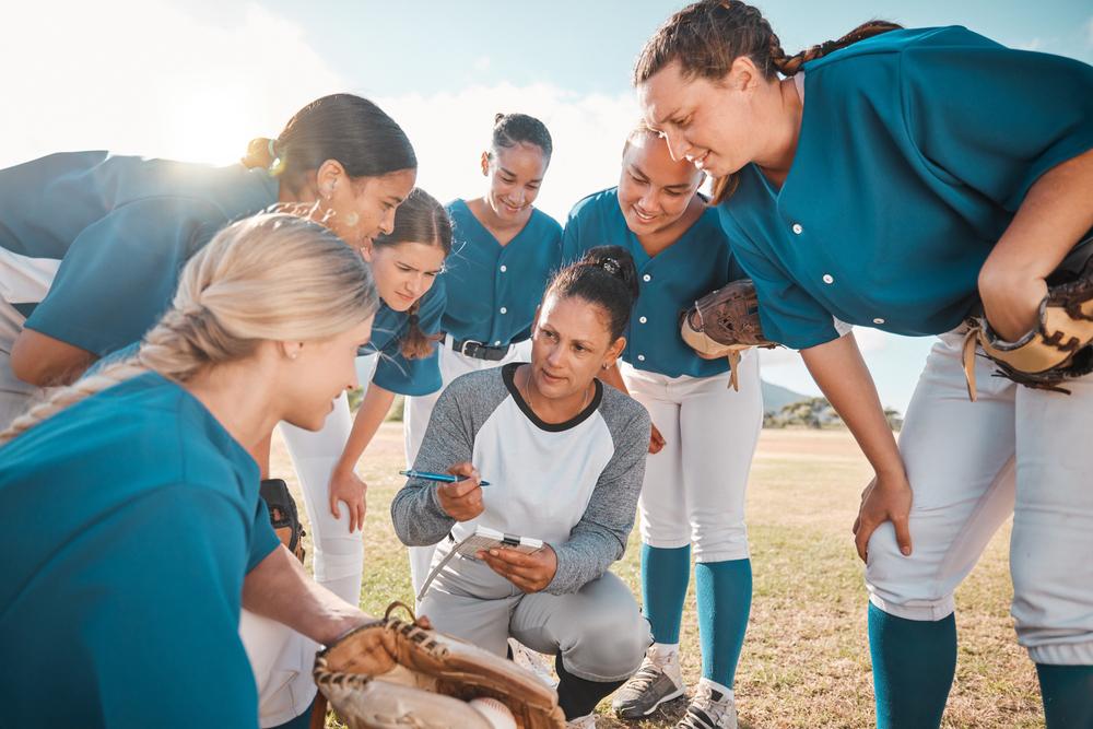 Female coach with teen girl softball team in a huddle.