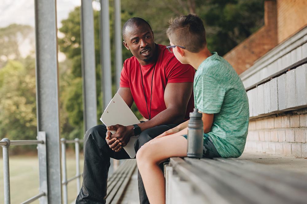 Coach talking to a young man on the bleachers.