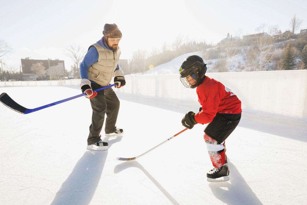 Youth sport hockey coach with athlete on outdoor rink.