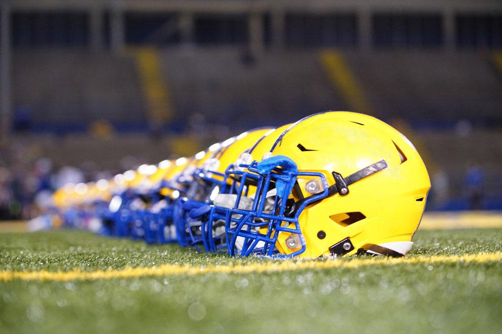 Yellow football helmets lined up in a row on a field.