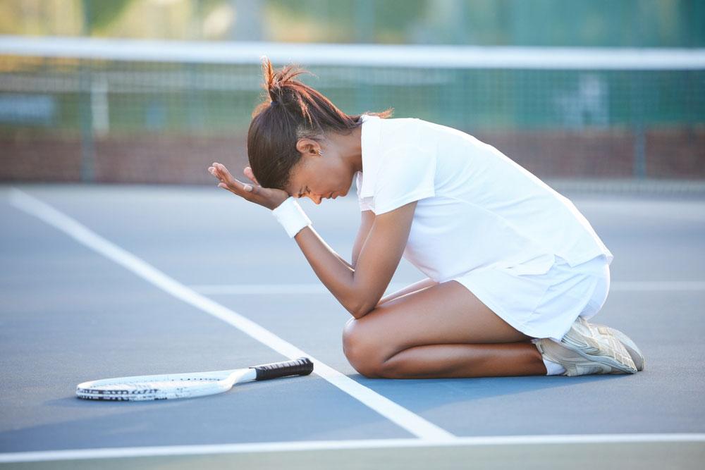 Young woman on knees on tennis court upset.