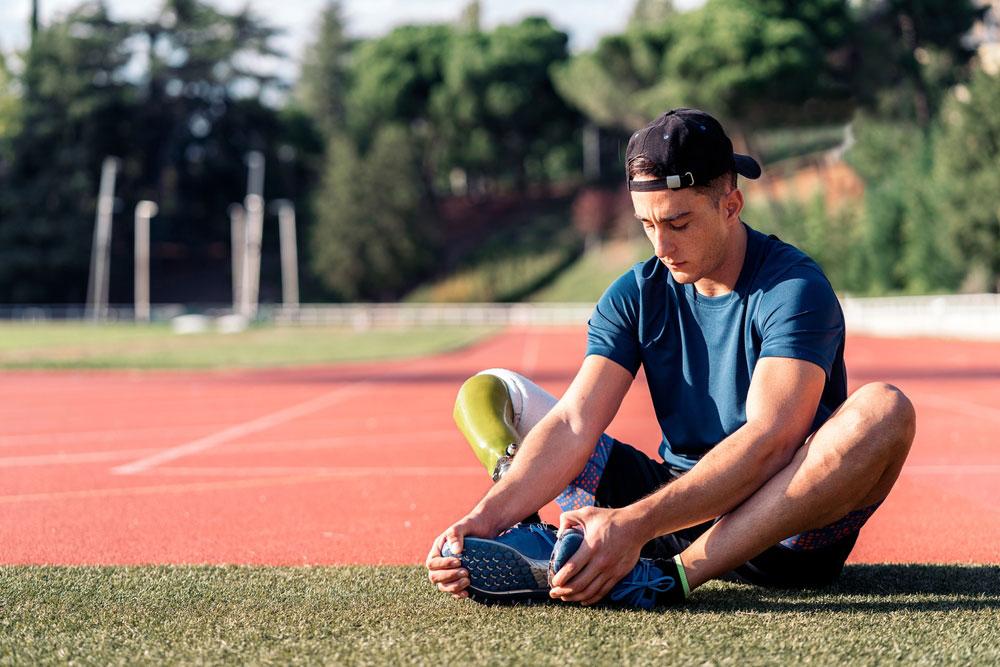 Young man with prosthetic leg streching near track.
