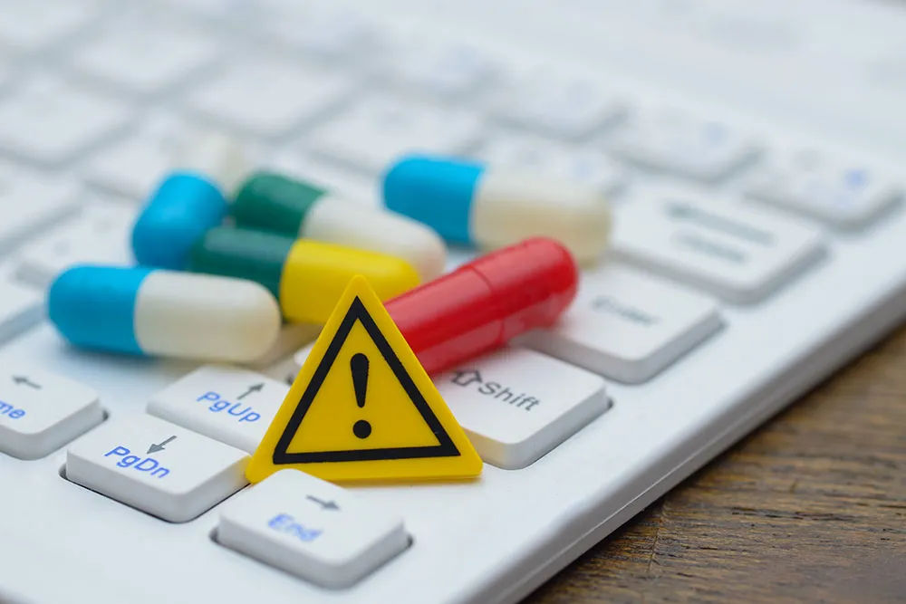 A warning symbol and pills sitting on a computer keyboard.