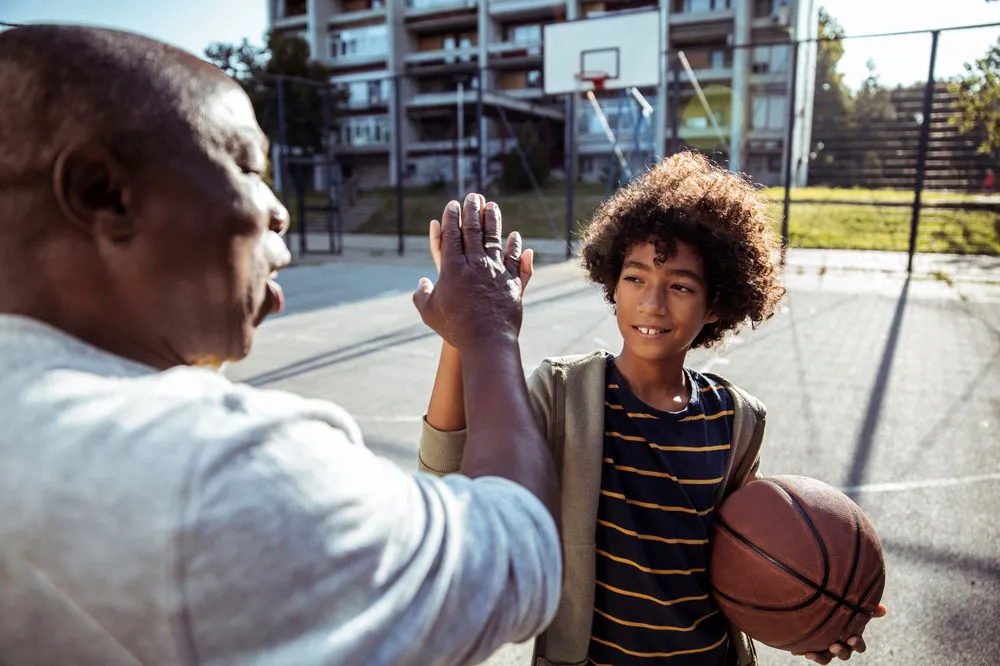 Young man high fiving his grandfather on a basketball court.