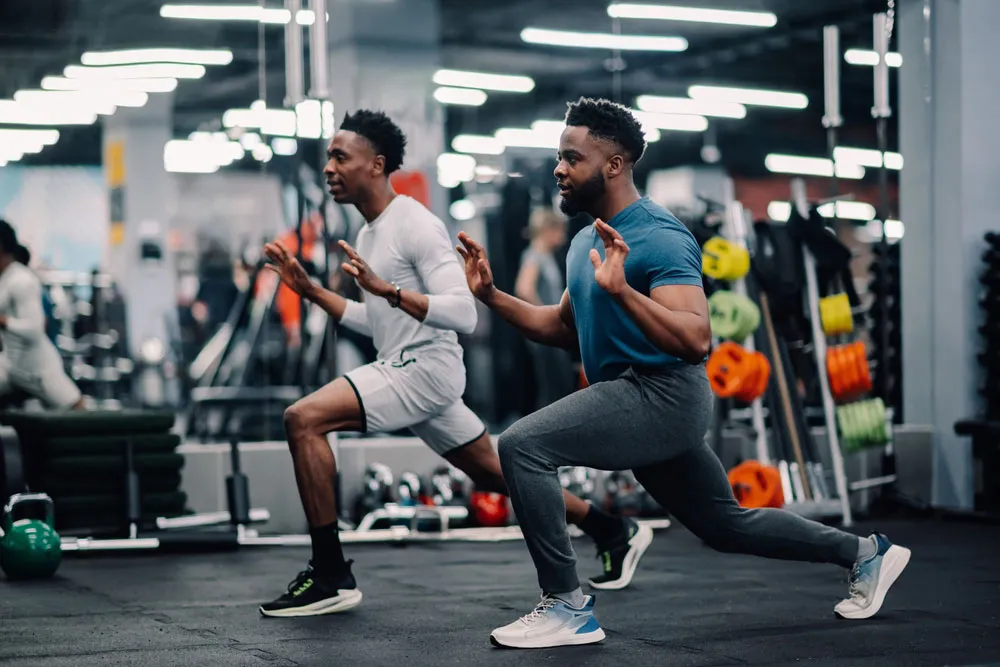 An athletic trainer working out with a young male athlete in a gym.