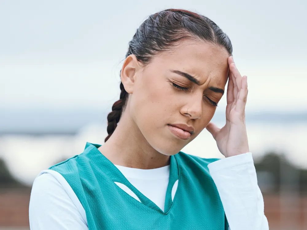 Female athlete grimaces in pain and rubs her forehead.