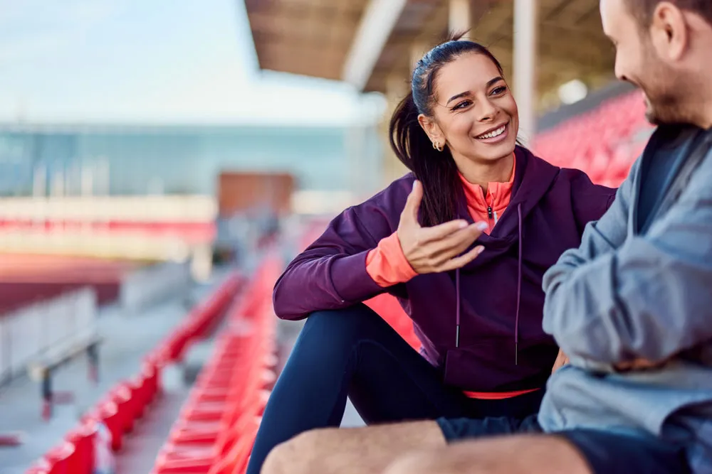 A woman and man talking in a sports stadium.