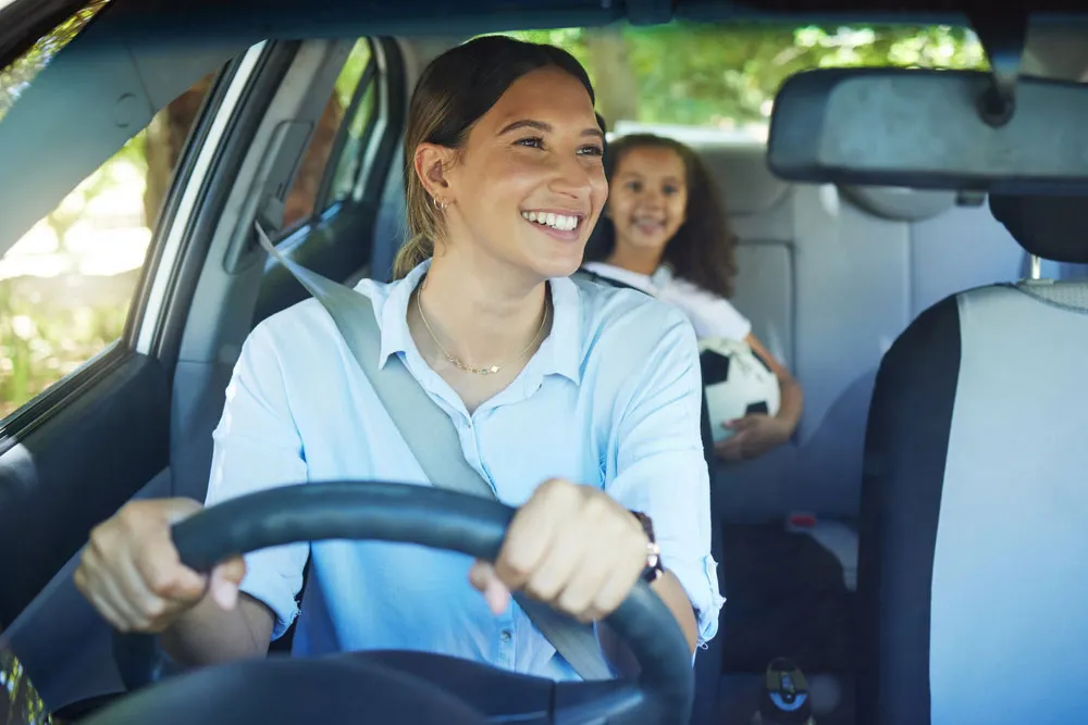 Mom driving daughter who is holding a soccer ball in backseat.