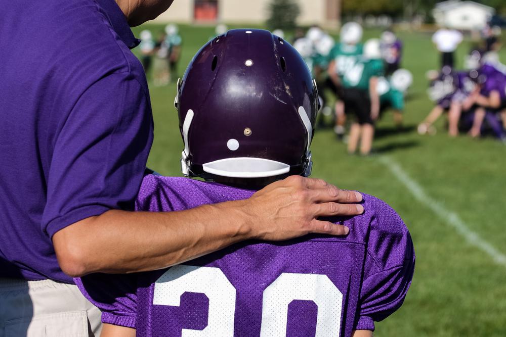 Football coach with arm around young athlete.