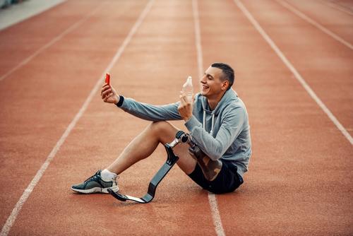 Male amputee on phone sitting on track.