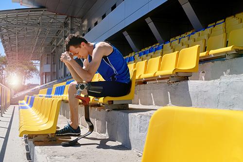 Leg amputee track athlete sitting in stands looking upset.