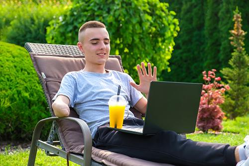 Young man with amputated arm sitting outside on laptop.