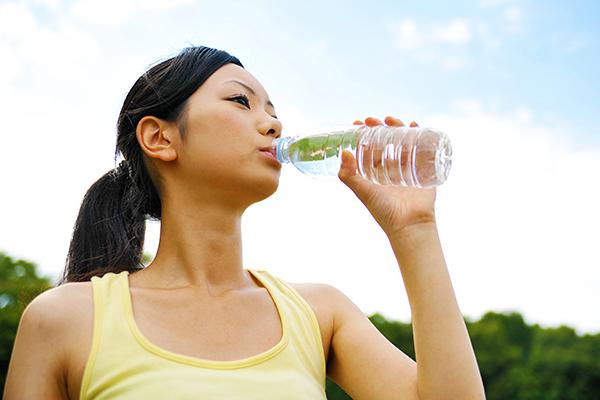 Asian girl drinking water out of a bottle.