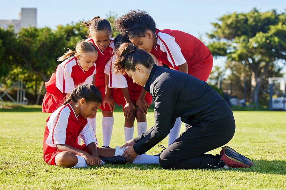 Coach tending to a youth female soccer athlete with injury, surrounded by team.