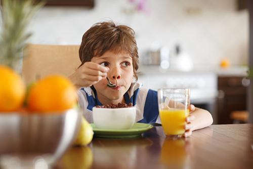 Young boy eating cereal and drinking orange juice.