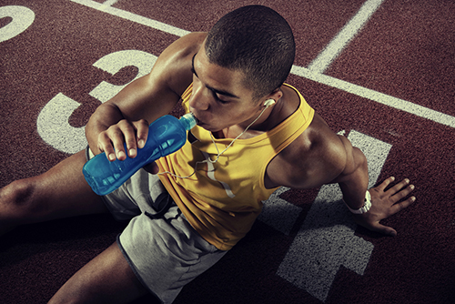 young man sitting on track drinking blue sports drink.