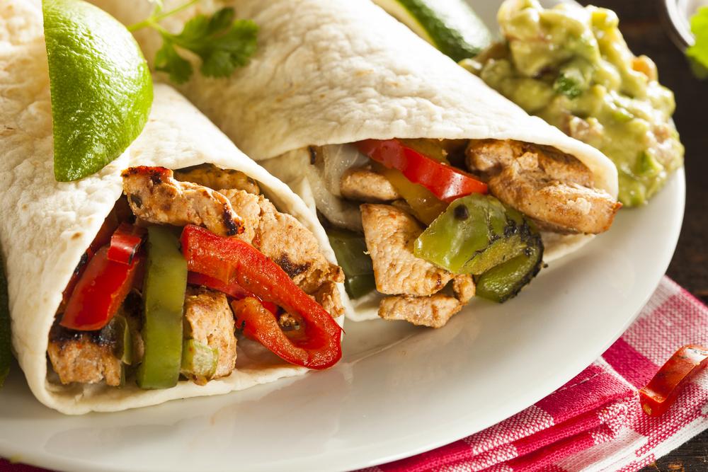 Close up of chicken fajitas in tortillas with a side of guacamole.