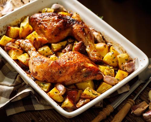 Chicken quarters over roasted vegetables in a pan.
