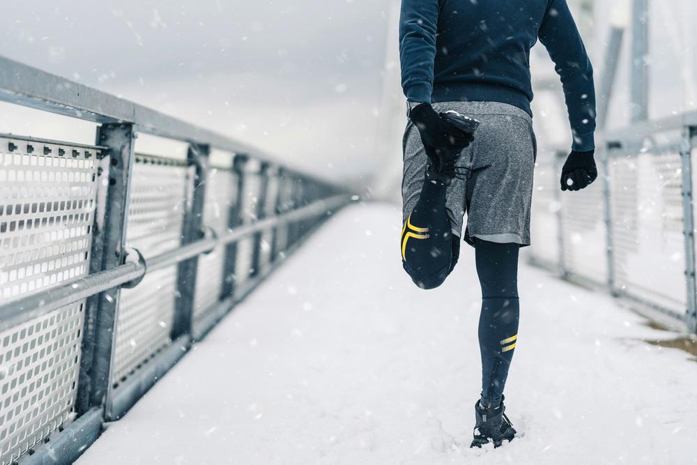 Man stretching thigh muscle before running outside in the snow.