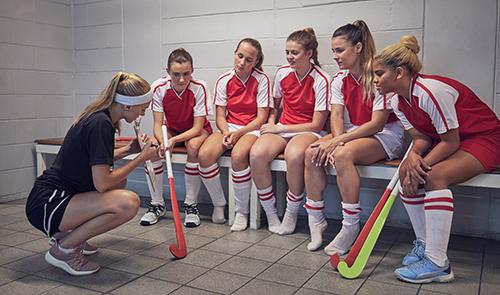 Coach talking to a girl's field hockey team in a locker room.