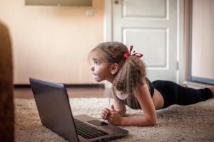 Young girl in workout clothes on laptop on ground indoors.